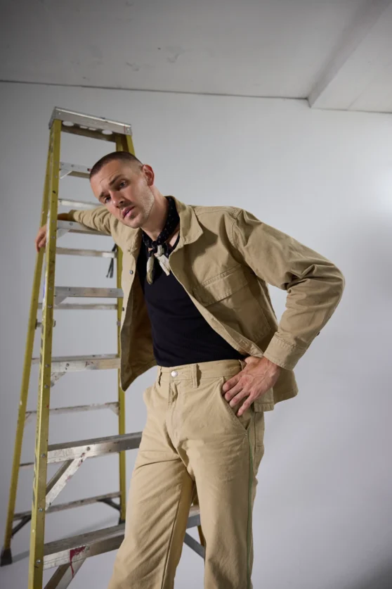 Male model in a beige suit striking a dynamic pose on ladder during a fashion photography session.