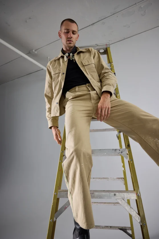 Studio fashion shoot featuring a male model on a ladder wearing a modern beige suit for ecommerce.
