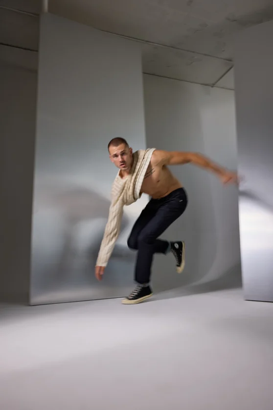 Side view of male model in navy jeans and cable knit sweater posing in clean studio for commercial ecommerce.