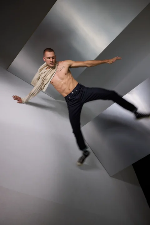 Side view of male model in navy jeans and cable knit sweater posing in clean studio for commercial ecommerce.