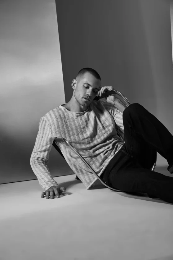 Fashion action shot of male model in cable knit sweater and dark trousers lunging in editorial studio.