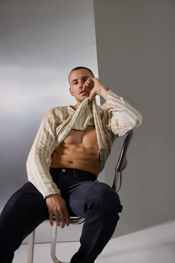Studio portrait of male model in a cream cable knit cardigan and navy trousers, styled for modern fashion editorial.