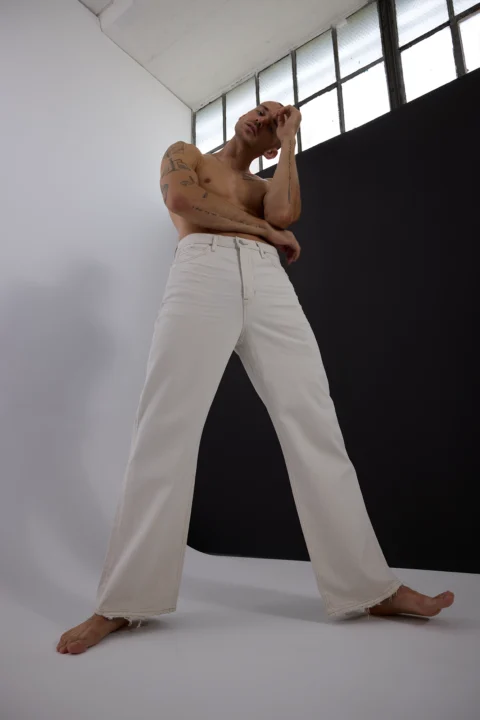 Male model posing in white pants against a minimalist studio background for commercial fashion photography.