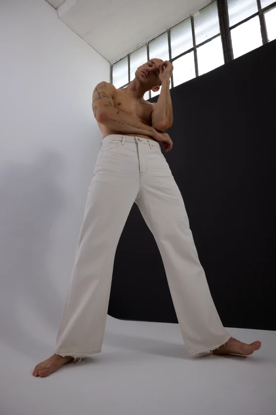 Male model posing in white pants against a minimalist studio background for commercial fashion photography.