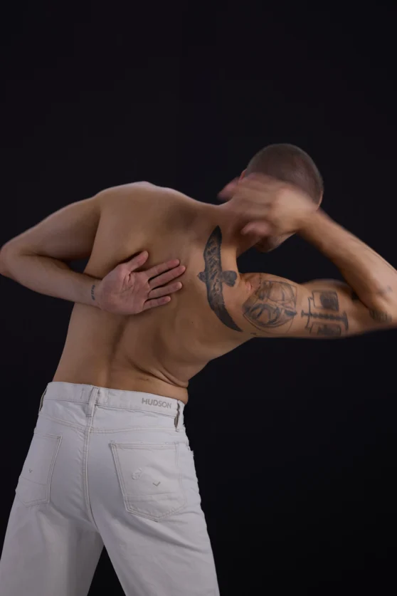 Commercial photoshoot with shirtless male model in dynamic pose wearing white pants.