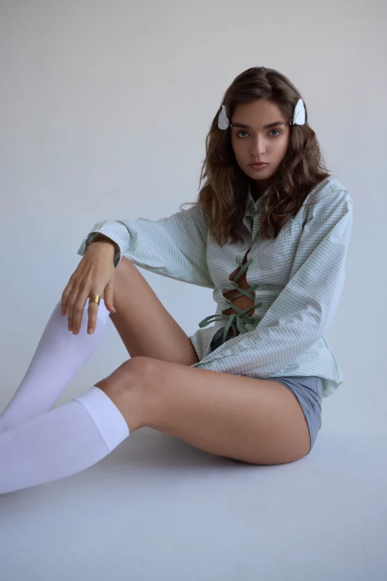 Seated model in knee-high socks and oversized shirt for commercial fashion shoot