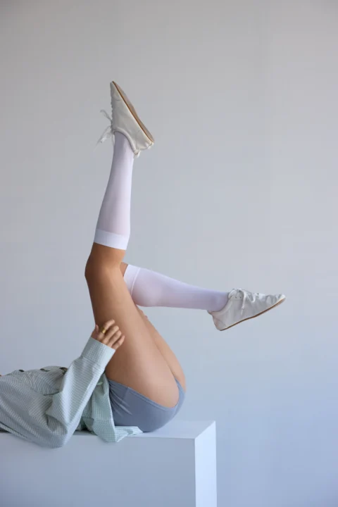 E-commerce photo showcasing white boots and knee-high socks against minimal background