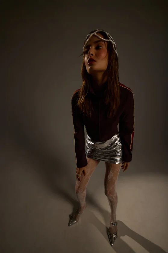 Fashion editorial model in silver mini skirt and dark top posing in studio lighting