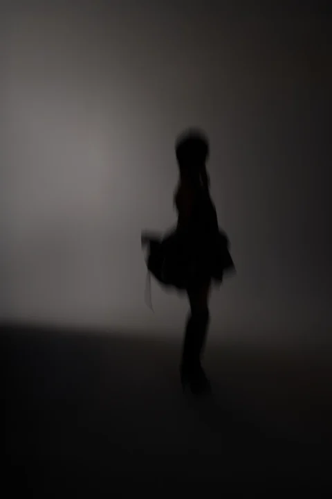 Stylized silhouette image of model walking in motion blur against neutral backdrop